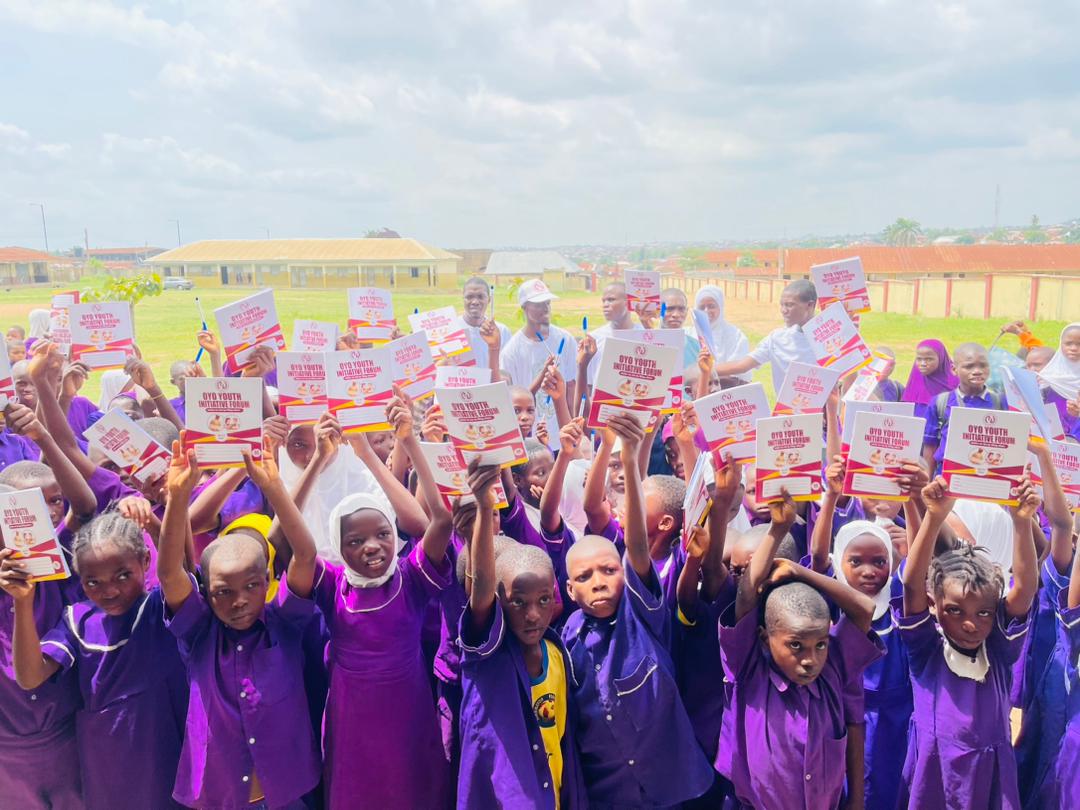 A large group of schoolchildren holding up OYIF notebooks